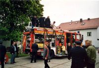 Das Fahrzeug steht mit ge&ouml;ffneten Rollos und ausgefahrenem Lichtmast auf dem Dorfplatz und wird von verschiedenen Leuten begutachtet.